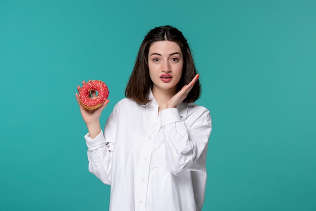 Schattig meisje jong mooi schattig brunette meisje in wit overhemd zwaaiende handen denken om donut te eten