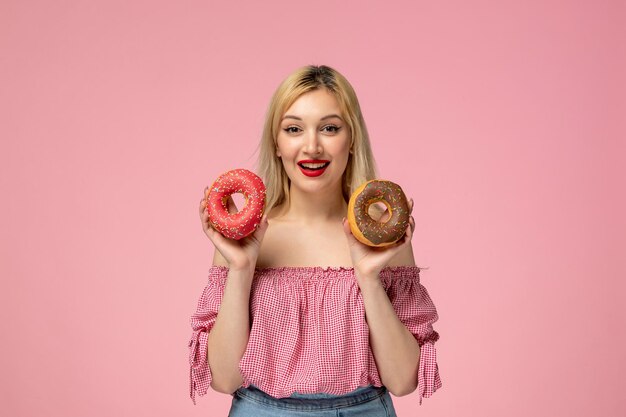 Schattig meisje schattige blonde meid met rode lippenstift in roze blouse blij lachend met donuts