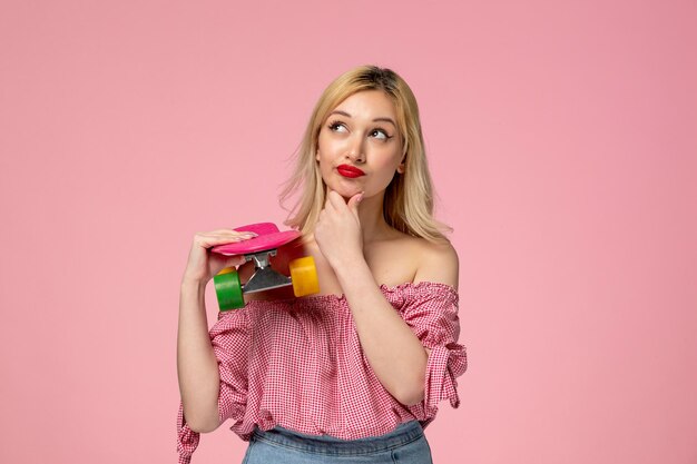 Schattig meisje schattige blonde meid met rode lippenstift in roze blouse denken en houden skateboard