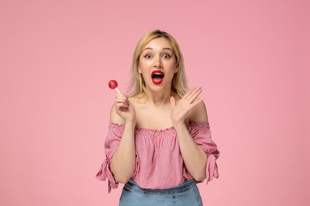 Schattig meisje schattige blonde meid met rode lippenstift in roze blouse zo opgewonden voor een lolly