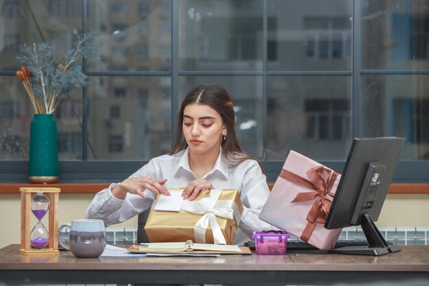 Schattig meisje zit aan het bureau en opent haar verjaardagscadeautjes Foto van hoge kwaliteit