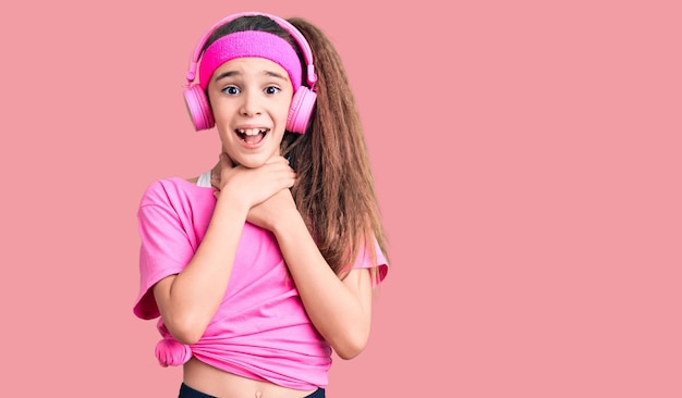 Schattig spaans kindmeisje dat gymkleding draagt en een koptelefoon gebruikt die schreeuwt en stikt omdat pijnlijk wurgen gezondheidsprobleem verstikking en zelfmoordconcept