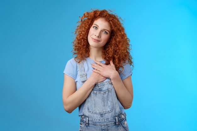 Schattig tedere aantrekkelijke roodharige krullend meisje koester romantische gevoelens dankbaar aangenaam geschenk aanraking hart druk handpalmen borst dankbaar glimlachend breed kantel hoofd blij gevoel liefdevolle zorgzame emoties.