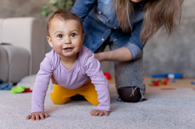 Gratis foto schattige baby kruipt op de grond met de hulp van zijn moeder