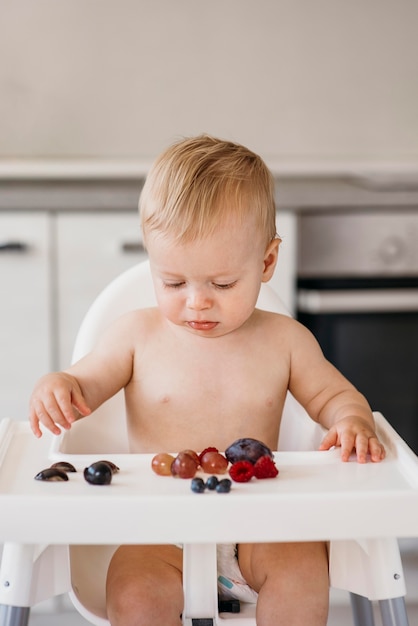 Schattige babyjongen in kinderstoel kiezen welk fruit te eten