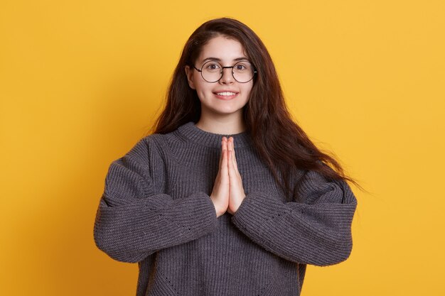 Schattige brunette jonge vrouw met mooi haar, handen bij elkaar te houden en te bidden.