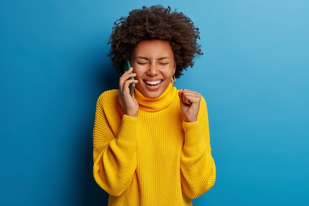 Schattige donkere huid volwassen vrouw gekleed in gele trui met behulp van mobiele telefoon met een gelukkige uitdrukking