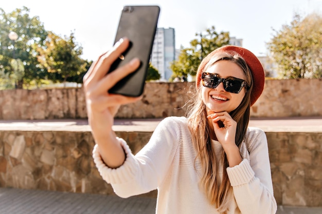 Schattige Europese vrouw in zwarte zonnebril chillen in goede herfstdag Outdoor shot van glamoureuze Franse grl selfie maken op straat
