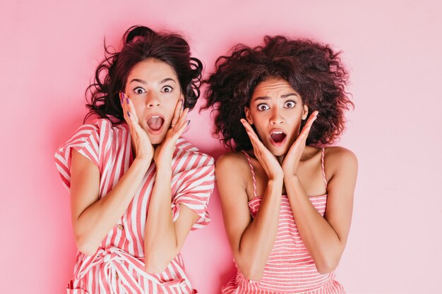 Schattige, jonge brunette meisjes met mooie ogen en zachte make-up, gekleed in roze gestreepte pyjama's, zeer bange gezichtsuitdrukkingen.