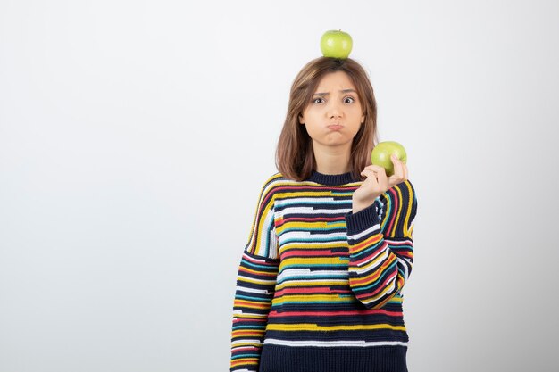 Schattige jonge vrouw die in vrijetijdskleding groene appels met droevig gezicht houdt.