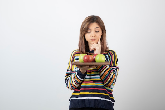 Schattige jonge vrouw die in vrijetijdskleding kleurrijke appels bekijkt.