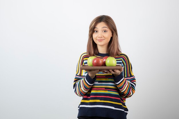 Schattige jonge vrouw die in vrijetijdskleding kleurrijke appels houdt.