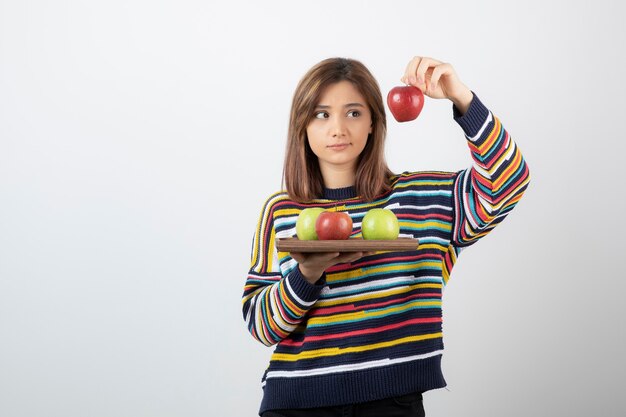 Schattige jonge vrouw in vrijetijdskleding met rode appels over witte muur.