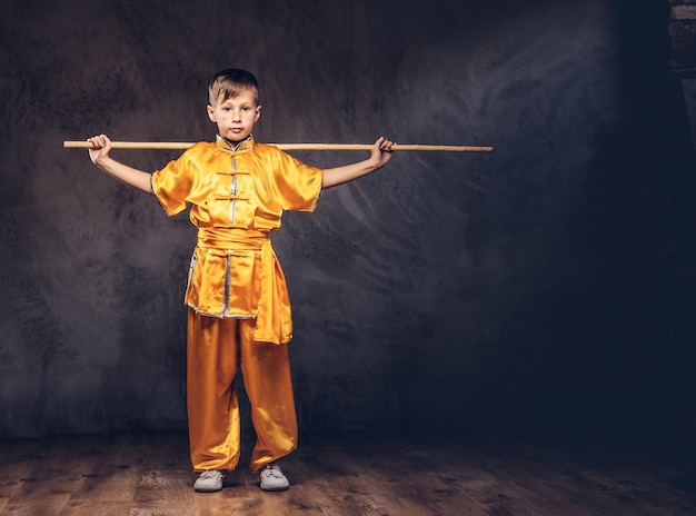 Gratis foto schattige jongen gekleed in het traditionele kostuum van een tibetaanse monnik toont de trucs met dao stick van het wellness-complex in de studio.