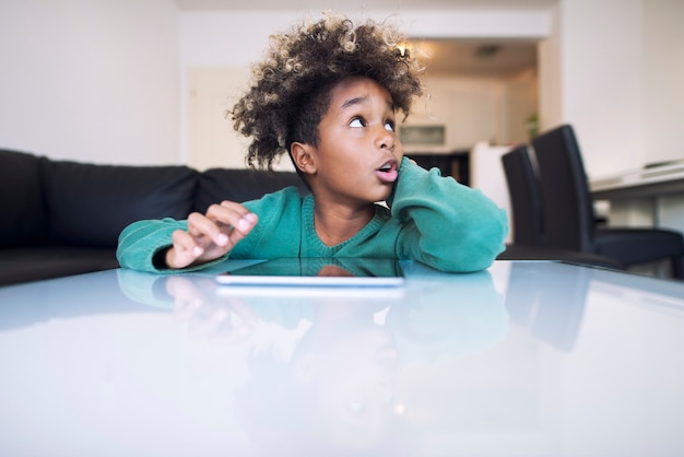 Schattige kleine afro meisje met grappig gezicht opzij kijken en surfen op het internet op haar tablet