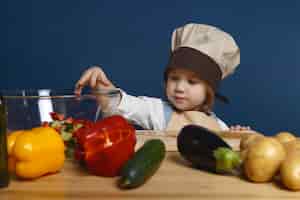 Gratis foto schattige kleine jongen met chef-kok hoed staan aan de keukentafel