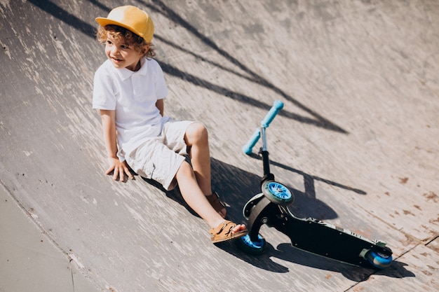 Schattige kleine jongen met krullend haar rijden scooter