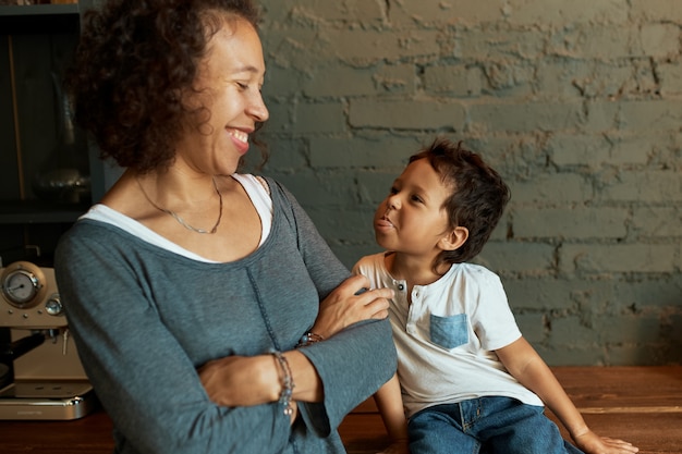 Schattige kleine jongen tong uitsteekt, zijn mooie jonge moeder breed glimlachend, samen plezier