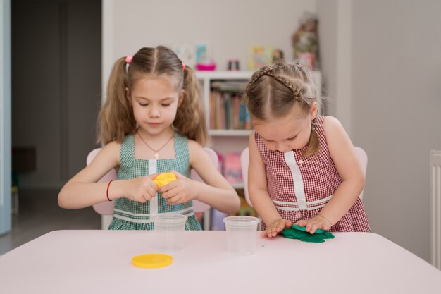 Schattige kleine meisjes gieten van plasticine op roze tafel