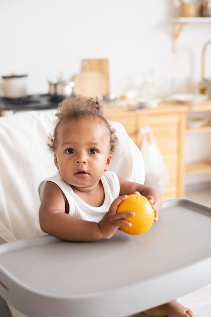 Schattige kleine zwarte baby die een sinaasappel vasthoudt