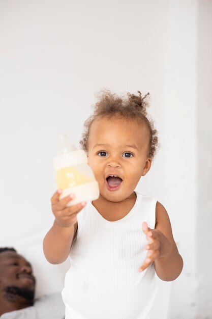 Schattige kleine zwarte baby die haar zuigfles vasthoudt