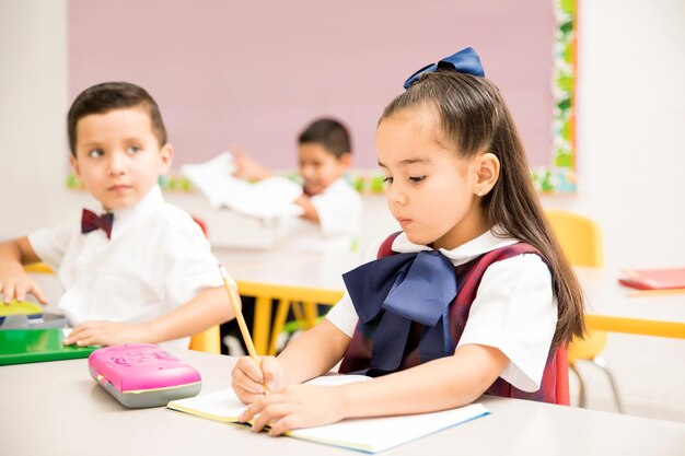 Schattige kleuters die een uniform dragen en een schrijfopdracht doen in een klaslokaal