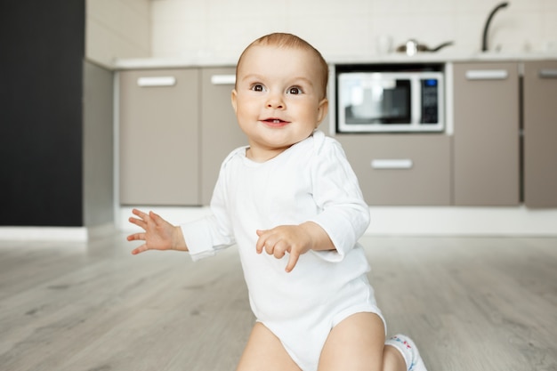 Schattige lachende baby zittend op de keukenvloer