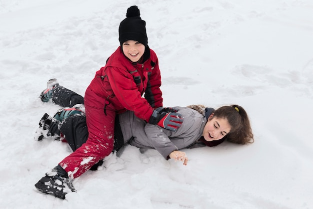 Schattige lachende jongen speelt met haar zus op besneeuwde grond op winterdag