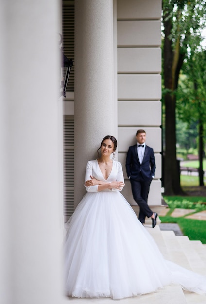 Schattige mooie jonge bruid vrouw in gezwollen elegante witte jurk poseren buitenshuis met bruidegom op achtergrond trouwdag fotosessie zomer ceremonie bruiden huwelijk
