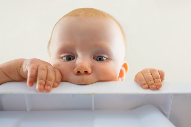 Schattige roodharige hongerige baby plastic bord bijten. Close-up beeld van nieuwsgierige pasgeborene op zoek vanaf tafel en vast te houden. Jeugd en kinderschoenen concept