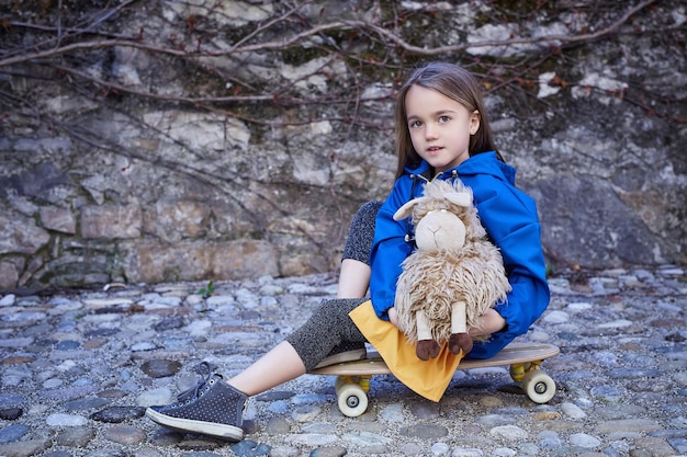 Gratis foto schattige tiener vrouw zittend op skateboard en flush speelgoed te houden over natuurlijke grijze achtergrond.