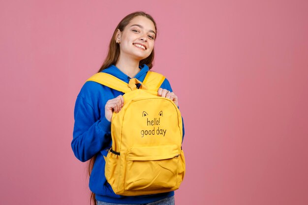 Schattige vrouw in blauwe blouse glimlachend naar de camera terwijl ze een grappige rugzak draagt en vice versa binnenshuis