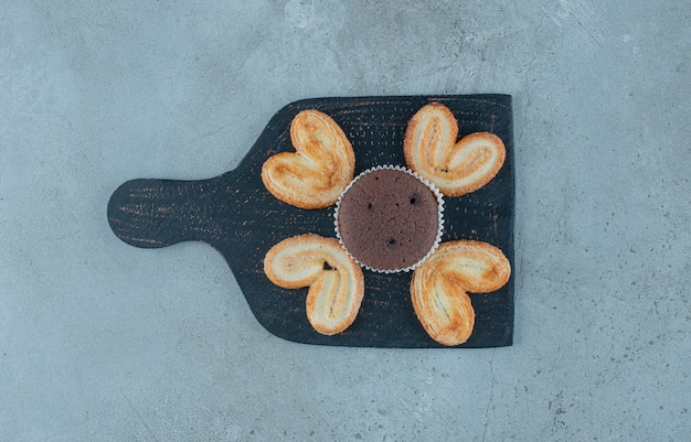 Gratis foto schilferige koekjes en een cupcake op een zwarte bord op marmeren achtergrond. hoge kwaliteit foto