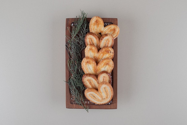 Schilferige koekjes opgesteld op een klein houten dienblad met een bundel van dennenbladeren op marmeren achtergrond.