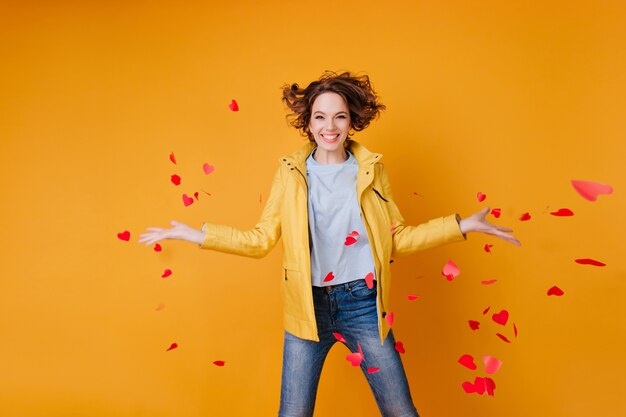 Schitterend vrouwelijk model dat papieren harten weggooit en geluk uitdrukt. Betoverende krullende vrouw die Valentijnsdag viert.