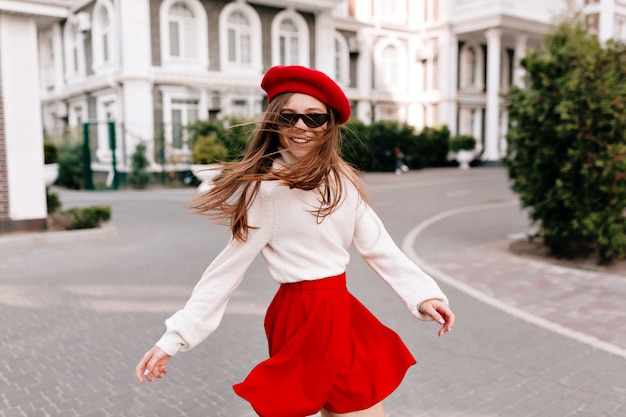 Gratis foto schitterende gelukkige vrouw met lang haar geklede rode rok en rode baret omdraaien