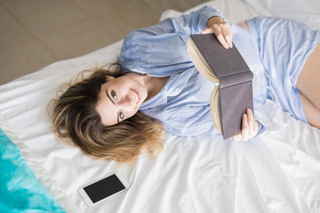 Schitterende jonge Spaanse vrouw die laat in bed blijft om een boek te lezen