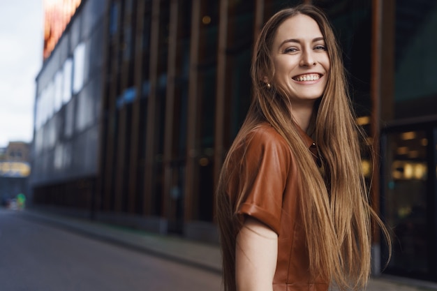 Schitterende jonge vrouw die bij camera glimlacht, zich achter omdraait en glimlacht.