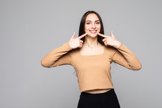 Schone en gezonde tanden. Jonge lachende mooie vrouw ik wijs vingers naar haar tanden op een grijze muur geïsoleerd.