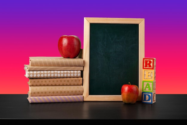 Schoolbord en gestapelde boeken tegen een gekleurde achtergrond