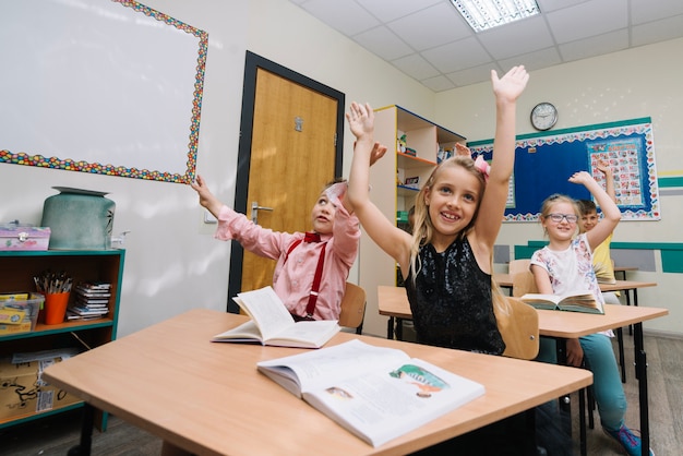 Gratis foto schoolkinderen zitten in klaslokaal houden handen omhoog