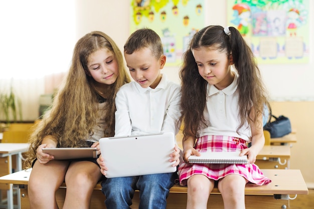 Gratis foto schoolkinderen zitten op bureau kijken naar tablet