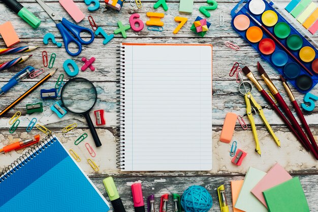 Schoollevering en notitieboekje op houten achtergrond.