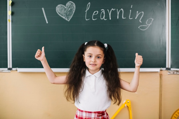 Schoolmeisje met handen omhoog op schoolbord