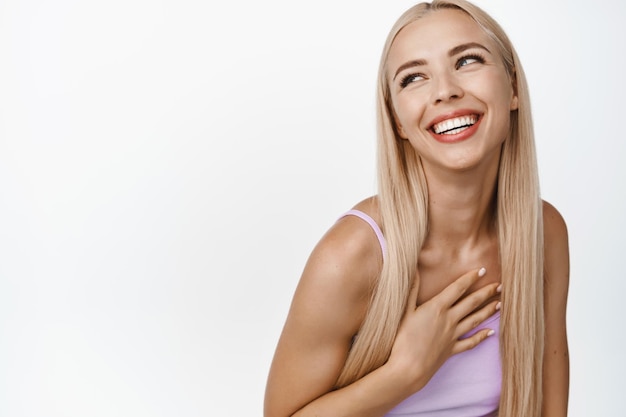 Schoonheid gelukkig openhartig meisje met blond lang haar dat lacht en opzij kijkt en op een witte achtergrond staat