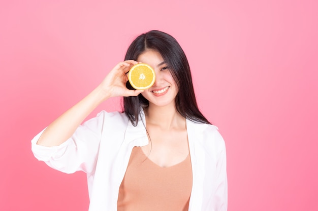 schoonheid vrouw Aziatische schattig meisje voelt gelukkig holdind oranje fruit voor een goede gezondheid op roze achtergrond