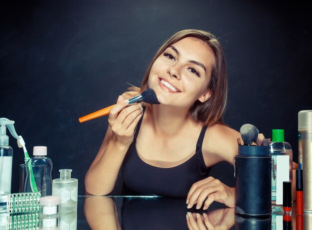 Schoonheid vrouw make-up toe te passen. Mooi meisje in spiegel kijken en cosmetica met een grote borstel toe te passen