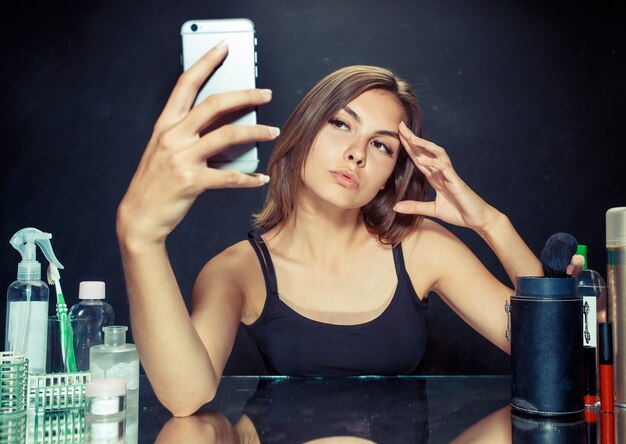 Schoonheid vrouw na het toepassen van make-up. Schoonheid vrouw met make-up. Mooi meisje kijken naar de mobiele telefoon en selfie foto maken. Kaukasisch model in de studio