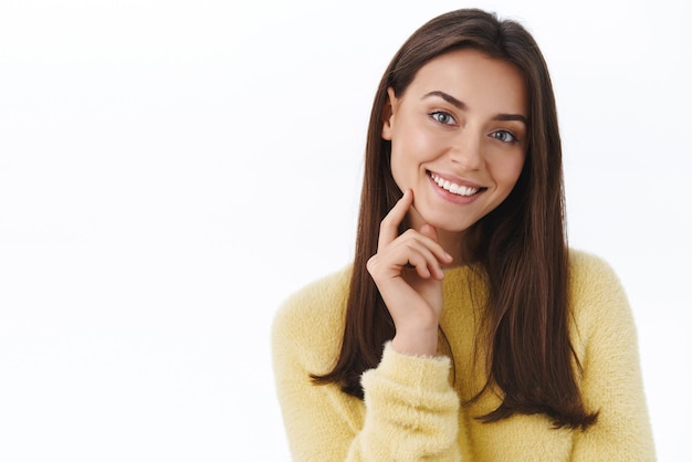 Schoonheid vrouwen gezicht concept close-up portret van mooie jonge moderne brunette vrouw zonder vlekken en make-up op zoek schattig aanraken kaak zachtjes glimlachend camera witte achtergrond