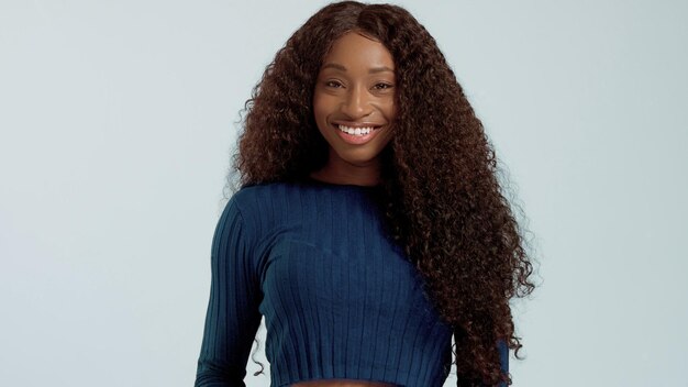 Schoonheid zwart gemengd ras Afro-Amerikaanse vrouw met lang krullend haar en perfecte glimlach camera kijken en glimlachend op blauw